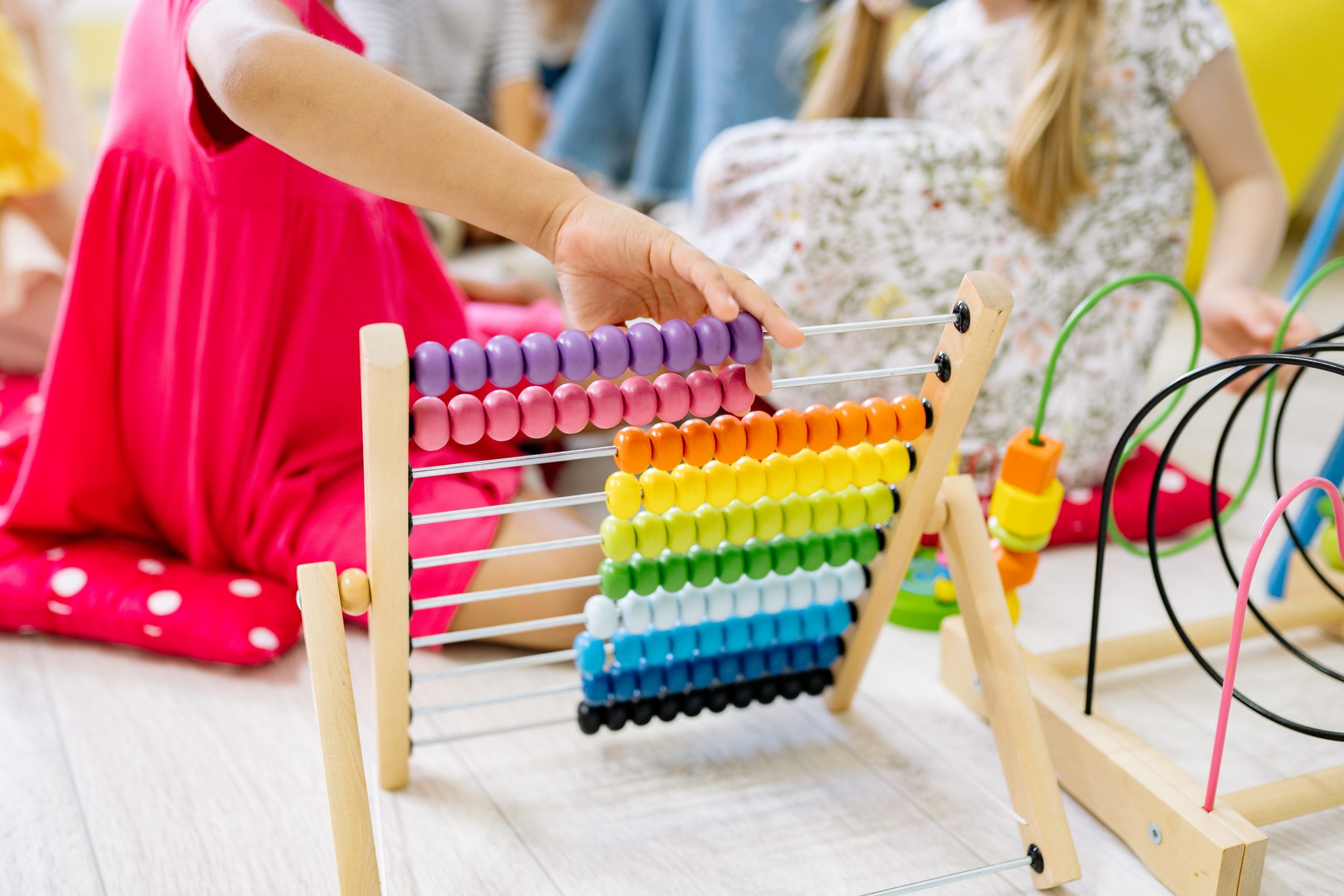 Child' arm moving pieces on an abacus with other children playing in background.